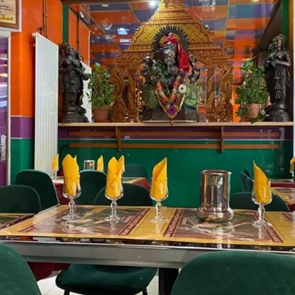 La salle de Krishna Bhavan: tables dressées, serviettes jaunes et murs orange, violets et verts